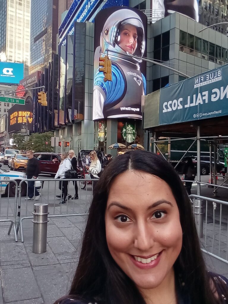 Rocket Women Founder, Vinita Marwaha Madill, in Times Square, NYC with herself wearing the Morgan Stanley Access I concept spacesuit on the screen behind her.